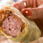 a close up of a sausage wrapped in cabbage with a bite taken out of it recipes