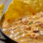 a close up photo of melted cheesy chorizo dip with taco chips being dipped