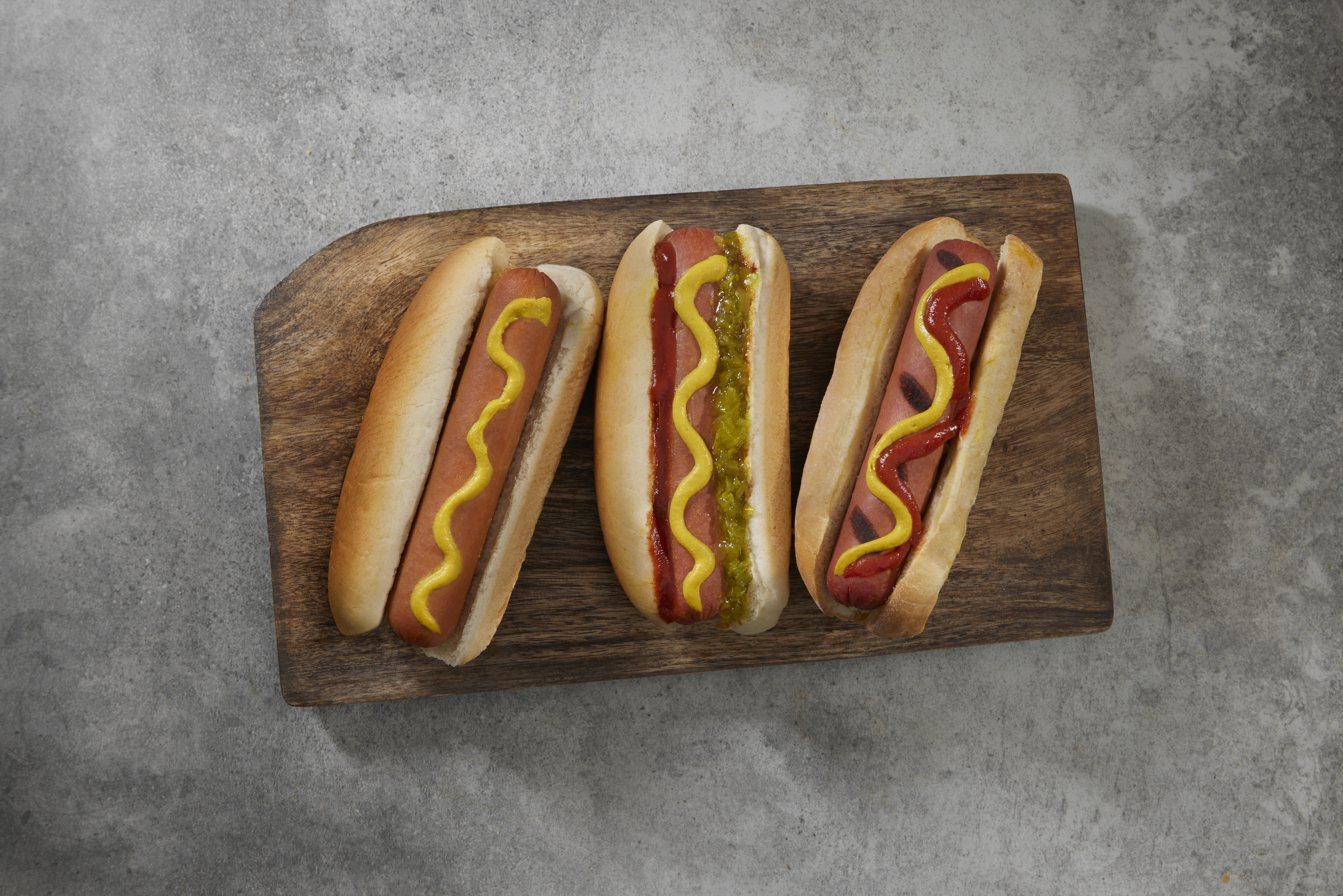 Three hotdogs with toppings on a wooden platter
